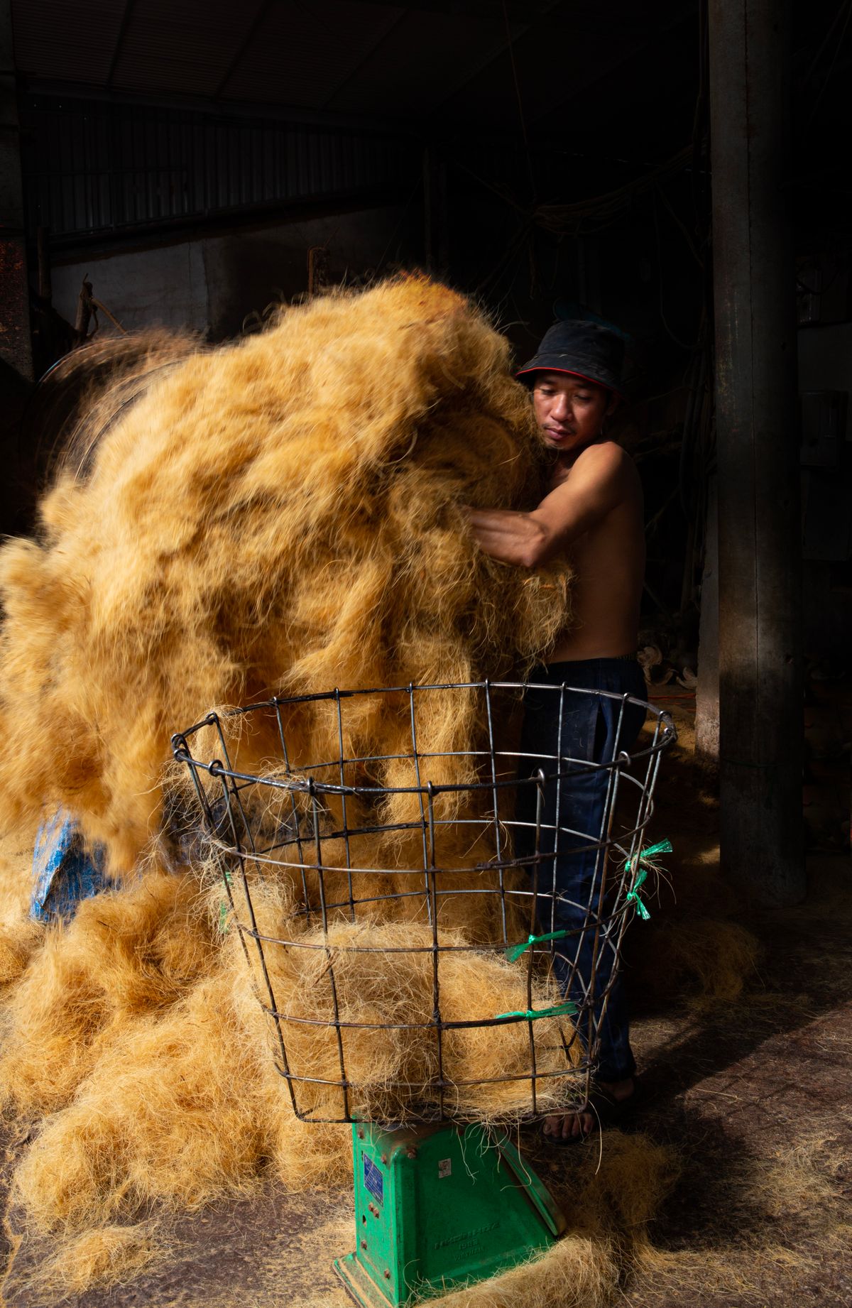 A worker gathering an armful of golden coco fiber inside an Indonesian coir factory